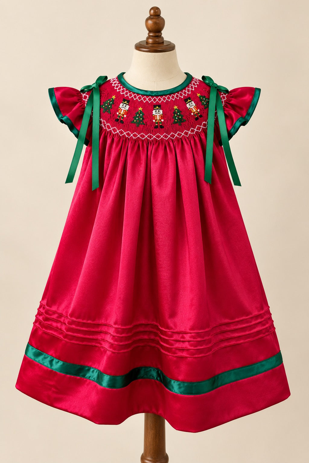 Front view of Big Bay, Little Bay’s red satin Nutcracker dress with embroidered smocking, green shoulder bows, and green hem trim.