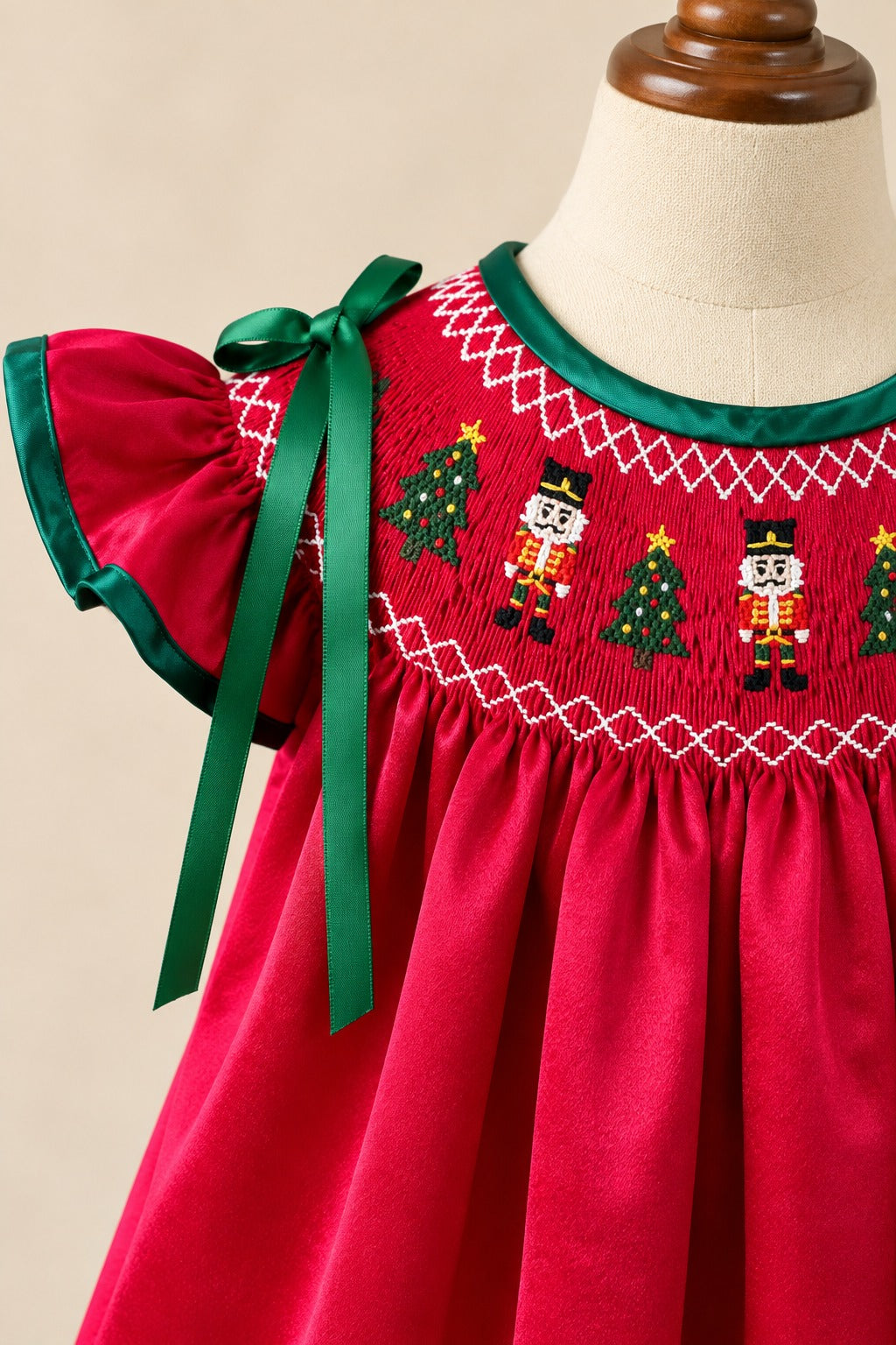 Close-up of nutcracker and Christmas tree embroidery on the red smocked bodice, with green neckline trim and a shoulder bow.